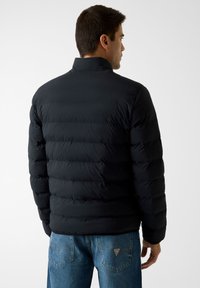 Schwarze Steppjacke mit horizontalen Nähten, hohem Kragen und glatter Textur, kombiniert mit hellblauen Jeans.