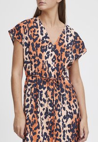 Abito a fantasia leopardo in arancione e blu navy, con scollatura a V, maniche corte, vita regolabile con nastro e dettagli con bottoni. Realizzato in tessuto leggero.