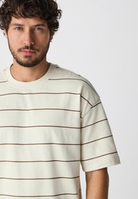Gestreept beige T-shirt van zachte stof met bruine horizontale lijnen, met een ronde hals en korte mouwen, ruime pasvorm, zonder zichtbare details.
