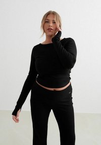 Crni dugi rukav uski top s rebrastom teksturom, uparen s odgovarajućim rastezljivim hlačama. Minimalistički dizajn bez vidljivih uzoraka ili hardvera.