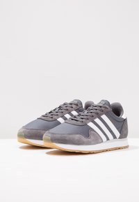 Pair of grey Adidas Haven sneakers with white stripes and gum soles on a white surface against a plain background.