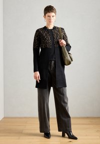 Czarny kardigan z górną częścią w leopardzi wzór, w komplecie z czarną bluzką i szarymi spodniami o szerokich nogawkach oraz czarnymi botkami na obcasie. Oliwkowa torebka na ramię.