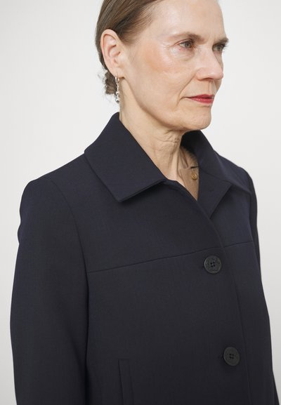 Manteau ajusté bleu marine avec un col structuré, deux boutons noirs et des poches latérales ; fabriqué en tissu texturé.