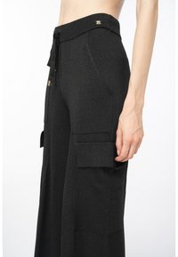 Zwarte wijde broek van gestructureerde stof, met een tailleband met trekkoord, zijzakken en accentzakken in cargostijl.