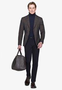 Brunternet blazer over en marineblå turtleneck, sorte bukser og brune lædersko. Bærer en struktureret brun taske med dobbelt håndtag.