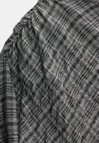 Tissu à carreaux gris et noir, texture tissée, présentant une apparence froissée, mettant en valeur des motifs variés et des fils en lignes entrecroisées.