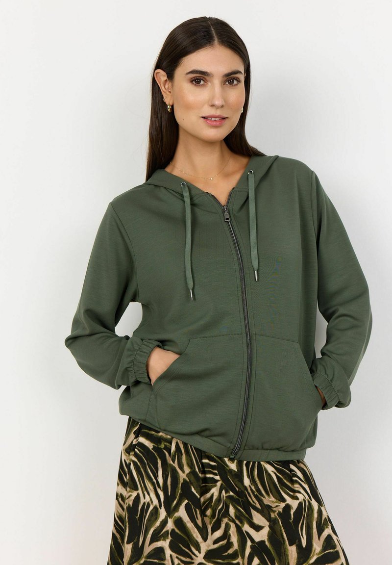 Zelená mikina na zips s kapucňou na šnúrku, elastickými manžetami a prednými vreckami, skombinovaná s patterned sukňou v prírodných odtieňoch.