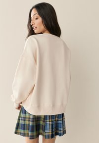 Sudadera holgada de color rosa claro con puños acanalados, combinada con una falda plisada de cuadros en tonos azul, verde y amarillo.