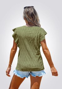 Top corto a maniche corte color verde oliva con motivo a diamante testurizzato, abbinato a pantaloni shorts in denim leggero azzurri con frange. Nessun logo o etichetta visibile.