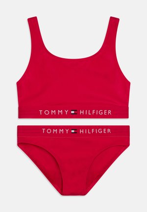 Röd bikini-set med en ärmlös topp och matchande trosor. Band med "TOMMY HILFIGER"-logotyp i kontrasterande färger. Slät, elastisk tyg.
