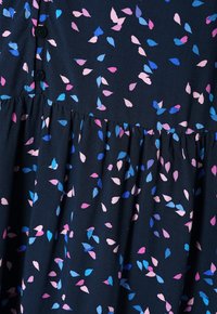 Donker marineblauwe stof met verspreide roze en blauwe bladdessins, voorzien van een knopenpatroon en een geplooide onderkant. Zachte textuur met een vloeiende vormgeving.