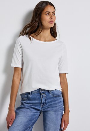 T-shirt blanche à manches courtes avec un large décolleté, fabriquée en tissu doux, associée à un jean en denim bleu clair avec un design standard à cinq poches.