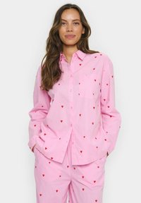 Camicia rosa con bottoni e maniche lunghe, con taschino e un motivo di piccoli cuori rossi, realizzata in un tessuto leggero.