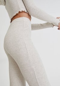 Leggings côtelés beige clair avec une coupe ajustée, taille haute et détail de couture latérale, associés à un top court avec des bords à volants.