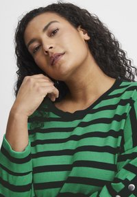 Zeleno-črna prugasta pletena jopica, okrogla ovratnika, ohlapen kroj, z rebrastimi manžetami in gumbi na rokavih. Mehka tekstura, sproščen dizajn.
