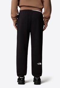 Svarta joggingsbyxor med elastisk midja, med en liten vit logotyp på nedre delen av vänster ben. Tyget verkar mjukt med en avslappnad passform.