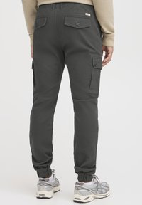 Svarta cargobyxor med elastisk midja, bakfickor med knappar och smalnande anklar, tillsammans med grå sneakers.