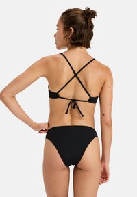 Black bikini with cross-back straps and tied closure. High-waisted bottoms. Smooth texture, minimal design with no visible patterns or accents.