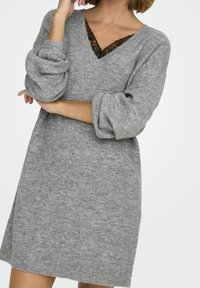 Robe pull en tricot gris avec un décolleté en V, doté d'un sous-vêtement en dentelle noire, de longues manches bouffantes et une coupe décontractée, mise en valeur par une texture douce.