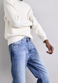 Krämfärgad ribbat stickad tröja som är kombinerad med ljusblå denimjeans, med en avslappnad passform och blekt tvätt. Enkelt mönster med subtila sömdetaljer.