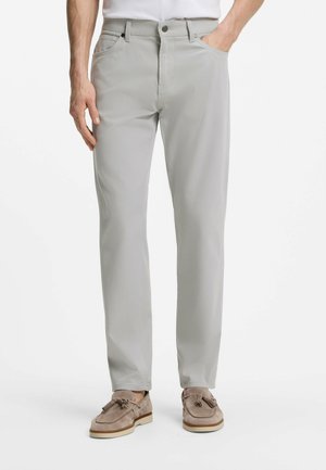 Mann trägt hellgraue gerade geschnittene Hose mit Taschen und beige Tassel-Loafers vor weißem Hintergrund.