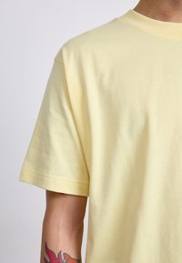 Trumpas rankovėmis geltonas medvilninis marškinėliai su apvaliu kaklu ir minkšta tekstūra, pasižymintis švariu kirpimu ir be matomų raštų ar akcentų.