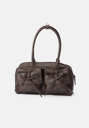 Brown leather handbag with two front pockets featuring ties, rounded handles, and a zip closure. Smooth texture with a subtle sheen.