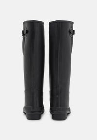 Bottes noires en caoutchouc hautes avec une texture lisse, des coutures verticales et des sangles latérales ajustables. Les semelles sont plates et durables.