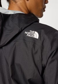 Čierna bunda s textúrovanou tkaninou, s výrazným bielym logom "The North Face" na pleci.