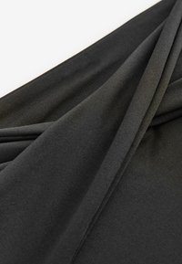 Nærbillede af sort ribstrikket stof foldet diagonalt på en hvid baggrund, der viser tekstur og fine strikkedetaljer.