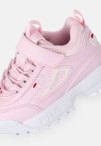 Bottines de sport roses avec tige synthétique, col rembourré, sangle Velcro et semelle blanche texturée avec motifs de traction.