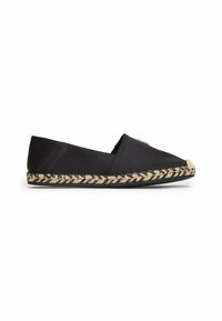 Espadrille noire à enfiler avec semelle en jute tissée et dessus lisse, avec un petit emblème métallique près des orteils sur fond blanc.