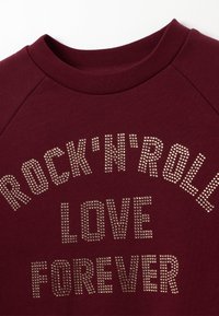 Sweatshirt bordeaux avec un col rond, orné de texte en strass "ROCK'N'ROLL LOVE FOREVER" sur la poitrine.