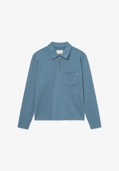 Garā piedurkne polo krekls blāvā zilā krāsā, ar rāvējslēdzēju, klasisku apkakli un krūšu kabatu. Izgatavots no mīkstas kokvilnas materiāla.
