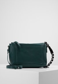 Teal läderaxelväska med en platt design, som har en framficka, flätad axelrem och dragkedjestängning.