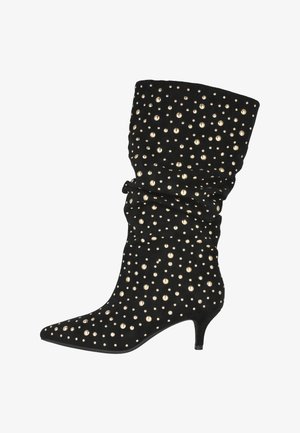 Botín de ante negro con un diseño arrugado, punta afilada y tachuelas doradas distribuidas uniformemente en la parte superior. Cuenta con un tacón kitten.