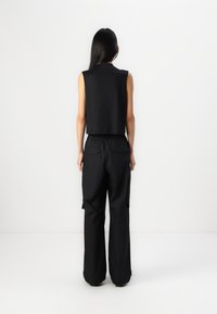 Μαύρο κοντό αμάνικο τοπ συνδυασμένο με χαλαρές μαύρες cargo παντελόνες που διαθέτουν πλευρικές τσέπες και κορδόνι στη ζώνη. Εμφανίζεται η πίσω όψη.