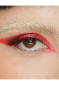 Primo piano di un occhio con iris marrone, lunghe ciglia nere e bold rossetto rosso che accentua la palpebra e l'arcata sopraccigliare. La texture della pelle è liscia.
