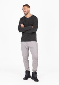 Donkergrijze T-shirt met lange mouwen en een gestructureerde afwerking, gecombineerd met lichtgrijze joggers en zwarte veterschoenen, staand in een neutrale omgeving.