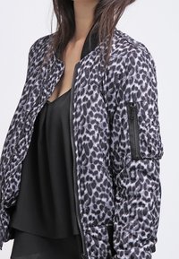 Chaqueta bomber con un estampado de leopardo en negro y gris. Cuenta con un cierre de cremallera en la parte frontal, cuello de canalé y un bolsillo lateral. Tela suave y ligera.