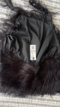 Black garment with a smooth fabric top and a textured, fluffy black fur bottom. Includes a care label with a barcode.