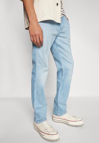 Lichtblauwe denim jeans met een rechte pasvorm, voorzien van contrasterende stiksel en zakken, gecombineerd met beige sneakers.