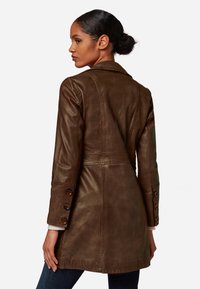 Brown leather trench coat with a tailored fit, buttoned cuffs, and a slightly textured surface. Features a classic collar and defined seams.