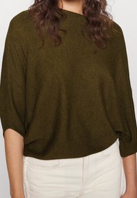 Olijfgroen oversized gebreid top met een gestructureerd ribpatroon en een brede, ronde halslijn, gecombineerd met lichte broeken.