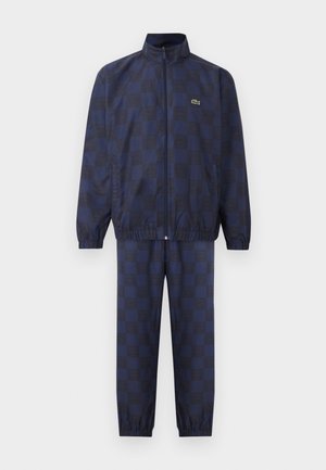 Navy tracksuit with checkerboard pattern. Lightweight fabric, zip-up jacket with high collar, and elastic waistband on pants. Lacoste logo accent.