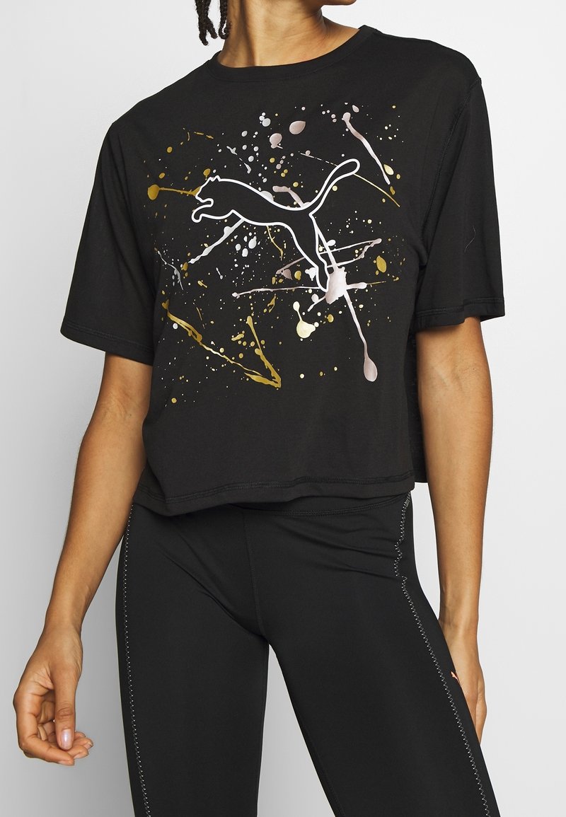 Černé krátké tričko z bavlny s bílou siluetou skákající kočky a barevnými skvrnami ve zlaté a růžové barvě.