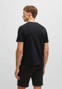 Schwarzes T-Shirt mit kurzen Ärmeln aus weicher Baumwolle und rundem Halsausschnitt. Es hat ein schlichtes Design und einen geraden Saum und wird mit schwarzen Shorts kombiniert.