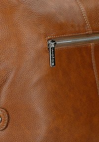 Brązowa skórzana torba o teksturowanej powierzchni, z metalowym suwakiem i metką z logo, podkreślająca swoje rzemiosło i trwałość.