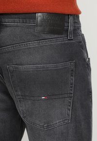 Czarne dżinsy z denimu z skórzaną metką Tommy Jeans w pasie oraz małym, trójkolorowym logo na tylnej kieszeni. Detale z przetarciami.