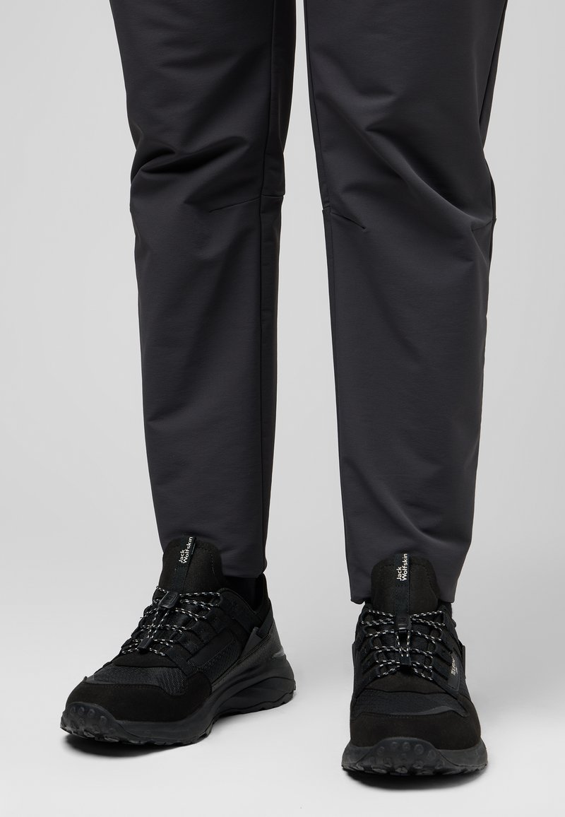 Schwarze Wanderschuhe aus strukturiertem Stoff, mit flachen Schnürsenkeln und Gummisohlen. Die Hose ist grau, mit glatter Oberfläche und tailliertem Design.